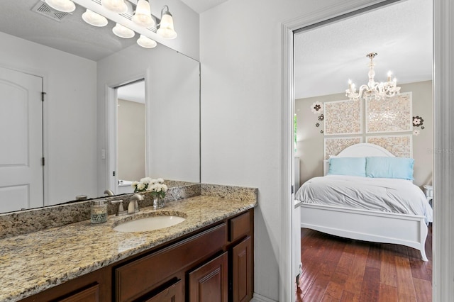 ensuite bathroom with vanity, wood-type flooring, an inviting chandelier, connected bathroom, and visible vents