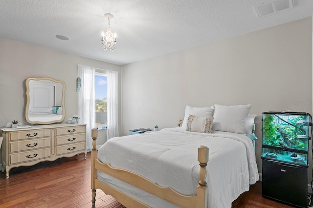 bedroom featuring visible vents, a notable chandelier, a textured ceiling, and wood finished floors