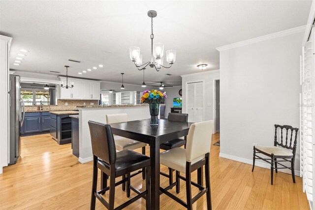 dining space featuring light wood-style floors, ceiling fan with notable chandelier, baseboards, and ornamental molding