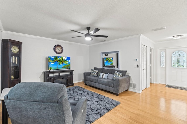 living area featuring ceiling fan, a textured ceiling, ornamental molding, visible vents, and wood finished floors