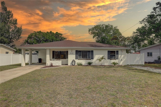 ranch-style home featuring concrete driveway, stucco siding, fence, a front lawn, and a carport