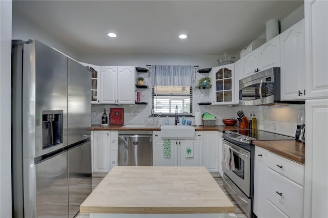 kitchen featuring a sink, open shelves, wooden counters, glass insert cabinets, and stainless steel appliances