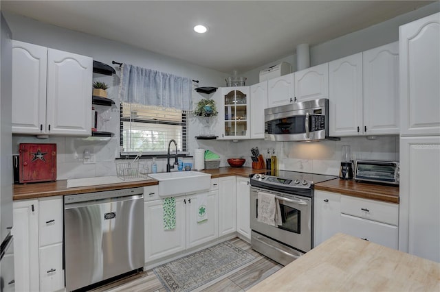 kitchen featuring a sink, stainless steel appliances, open shelves, and butcher block counters