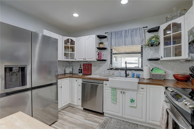 kitchen with a sink, open shelves, butcher block counters, stainless steel appliances, and white cabinets