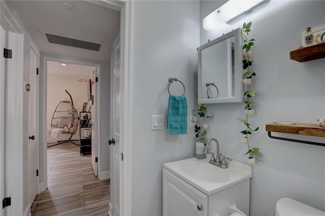 half bath featuring toilet, vanity, wood finished floors, and visible vents