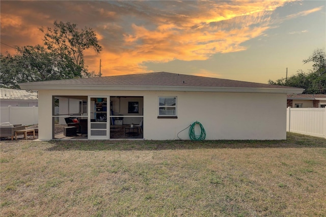 rear view of property with stucco siding, fence, and a yard