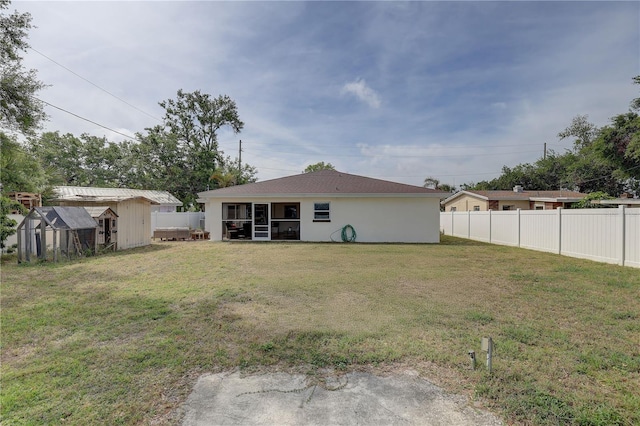 back of property with stucco siding, an outbuilding, a fenced backyard, a sunroom, and a yard