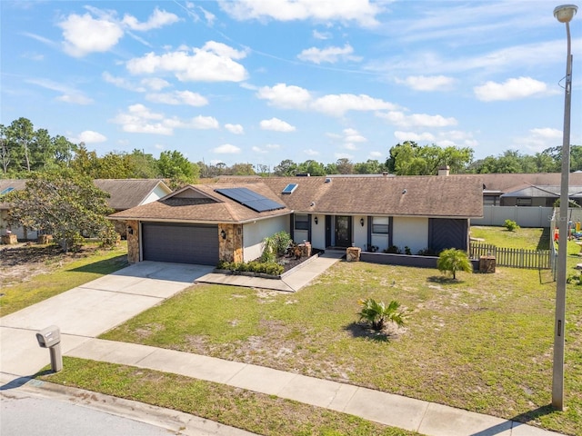single story home featuring driveway, an attached garage, a front yard, solar panels, and fence