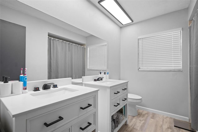 bathroom featuring two vanities, baseboards, toilet, a sink, and wood finished floors