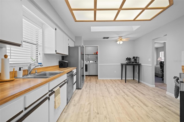 kitchen with butcher block counters, a skylight, appliances with stainless steel finishes, a sink, and washer and clothes dryer