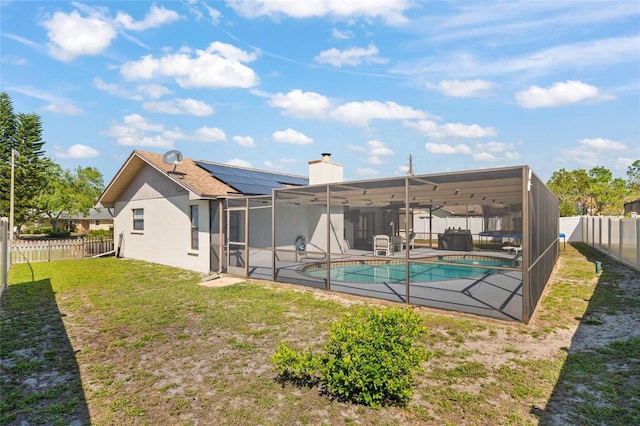 rear view of house featuring roof mounted solar panels, a fenced backyard, glass enclosure, a lawn, and a patio
