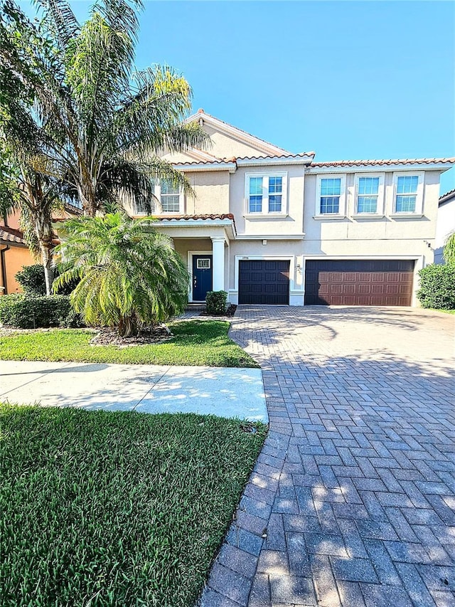 view of front of house with a garage, stucco siding, a tiled roof, and decorative driveway