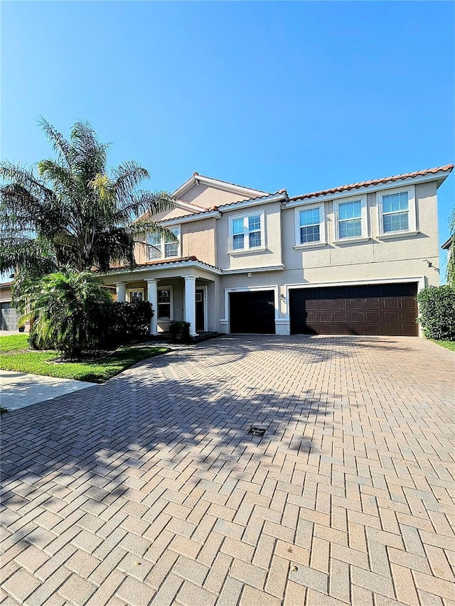 view of front of house featuring a tiled roof, decorative driveway, a garage, and stucco siding