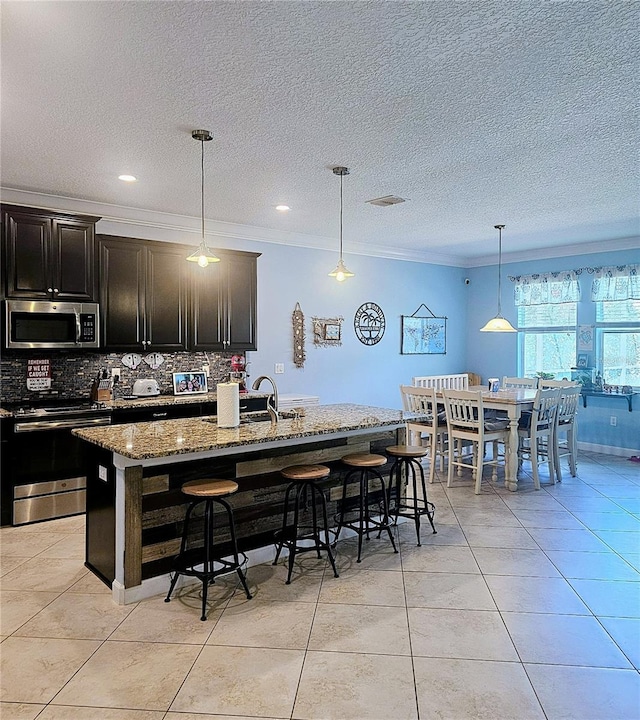 kitchen with appliances with stainless steel finishes, a kitchen breakfast bar, crown molding, decorative backsplash, and stone countertops