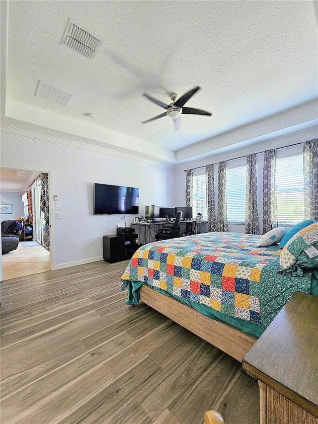 bedroom with a tray ceiling, a textured ceiling, visible vents, wood finished floors, and baseboards