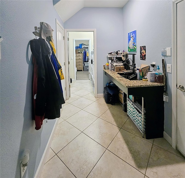 corridor featuring light tile patterned floors, baseboards, and vaulted ceiling