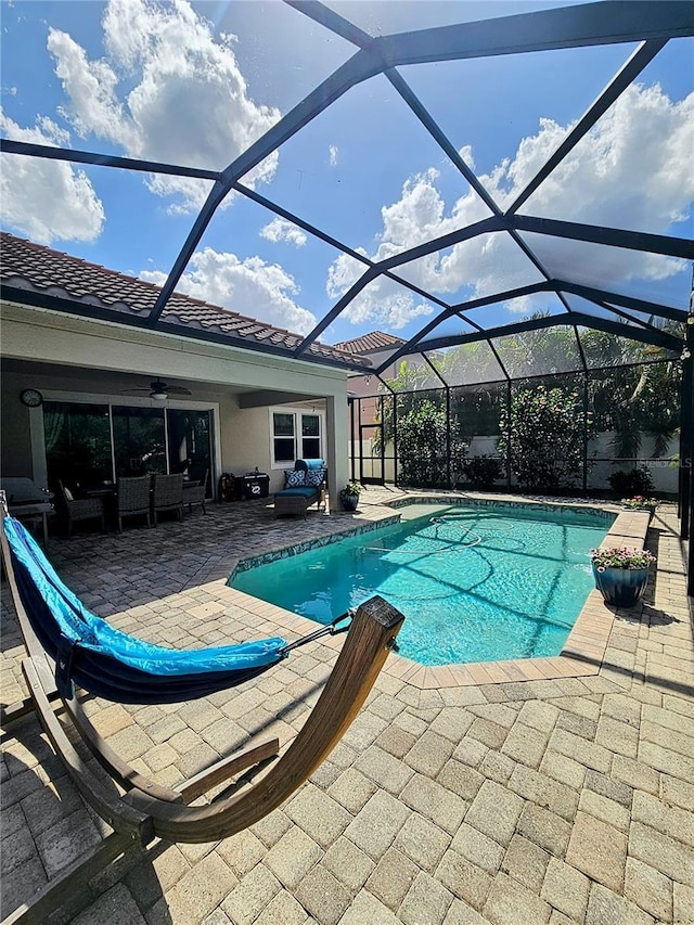 outdoor pool with an outdoor living space, a patio area, glass enclosure, and a ceiling fan