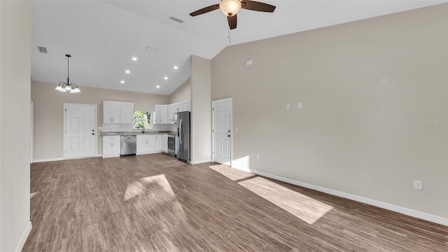 unfurnished living room with ceiling fan with notable chandelier, visible vents, wood finished floors, and baseboards