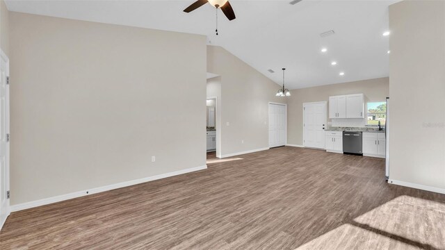 unfurnished living room with ceiling fan with notable chandelier, high vaulted ceiling, wood finished floors, and baseboards