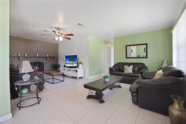 tiled living room with a textured ceiling, ceiling fan, visible vents, and a brick fireplace