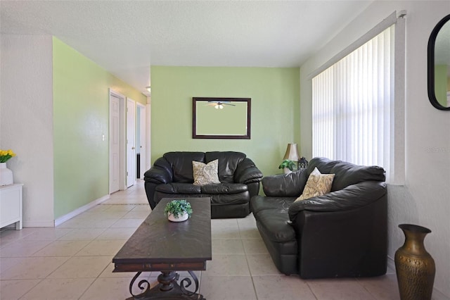 living area featuring a textured ceiling, ceiling fan, baseboards, and light tile patterned floors