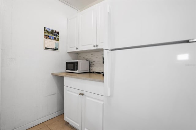 kitchen featuring light tile patterned flooring, white cabinets, light countertops, white appliances, and tasteful backsplash