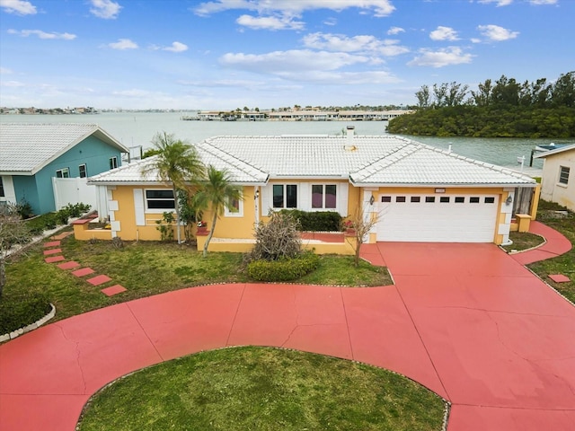 ranch-style house featuring a water view, stucco siding, driveway, a tile roof, and a garage