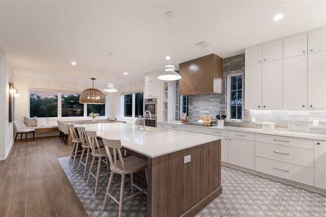 311 Spring Ave, Anna Maria, FL 34216 - kitchen with black electric cooktop, visible vents, a breakfast bar, a kitchen island with sink, and double oven