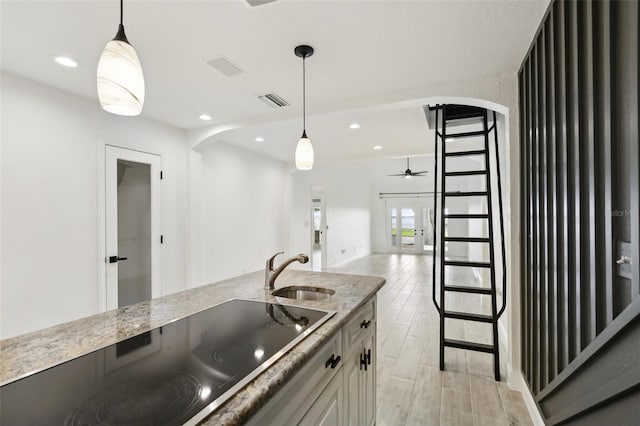 kitchen with wood finish floors, decorative light fixtures, visible vents, arched walkways, and a sink