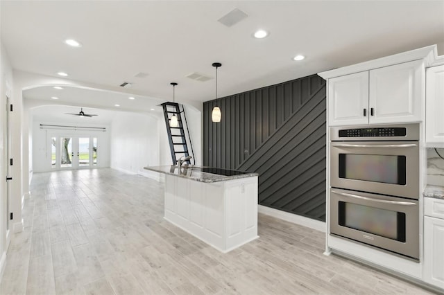 kitchen featuring white cabinetry, double oven, arched walkways, and light stone counters