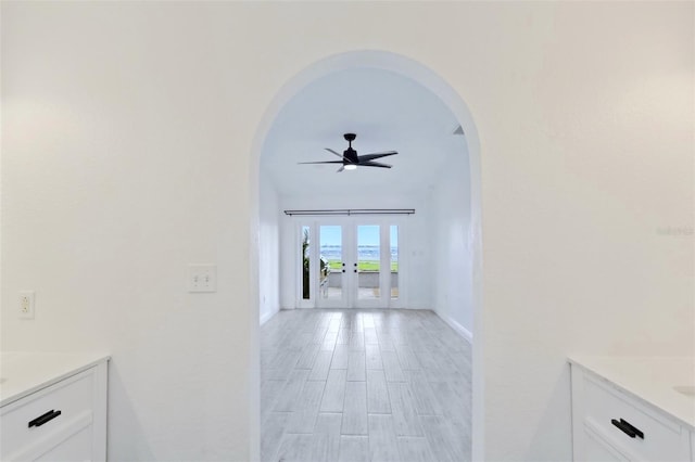hallway featuring french doors, baseboards, light wood finished floors, and arched walkways