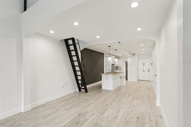 unfurnished living room with light wood-style flooring, arched walkways, baseboards, and recessed lighting