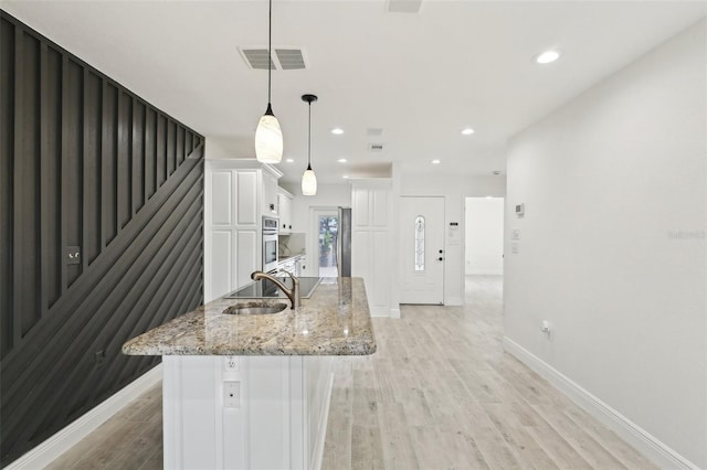 kitchen with light wood-style floors, light stone countertops, white cabinets, visible vents, and a sink