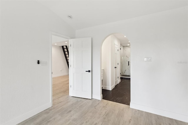 unfurnished room with arched walkways, wood finished floors, vaulted ceiling, and stairway