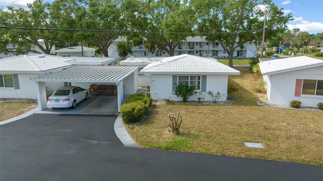 view of front facade featuring aphalt driveway, an attached carport, a tile roof, a front lawn, and stucco siding