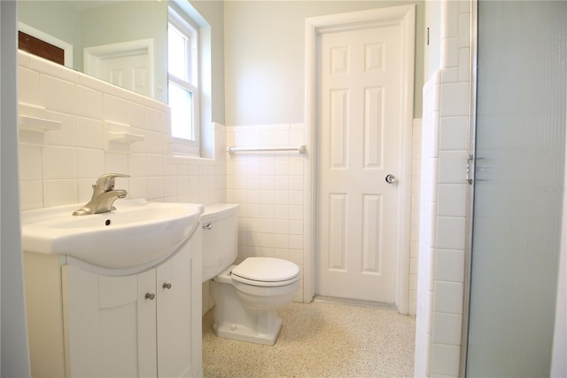 bathroom with a wainscoted wall, toilet, speckled floor, vanity, and tile walls