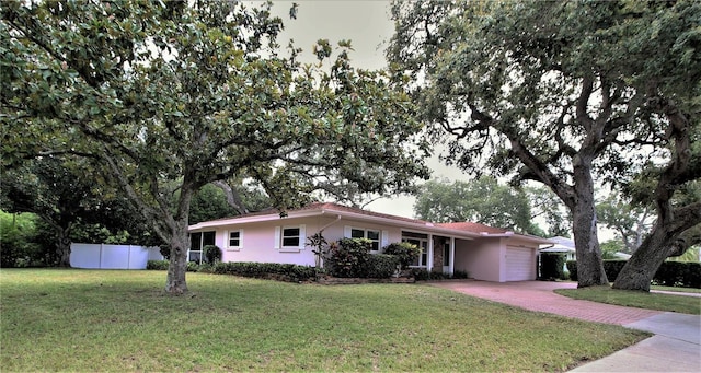 ranch-style house featuring driveway, fence, an attached garage, a front lawn, and stucco siding