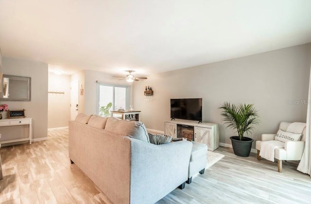 living area with baseboards, light wood-style floors, and ceiling fan