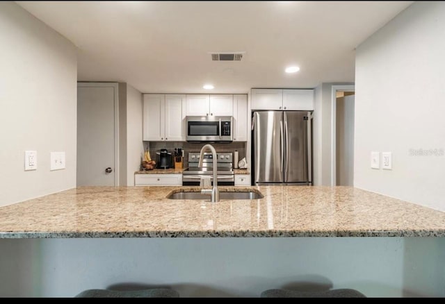 kitchen with light stone counters, a sink, stainless steel appliances, visible vents, and white cabinets