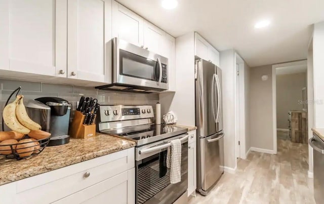 kitchen with white cabinets, light wood-style flooring, stainless steel appliances, and backsplash