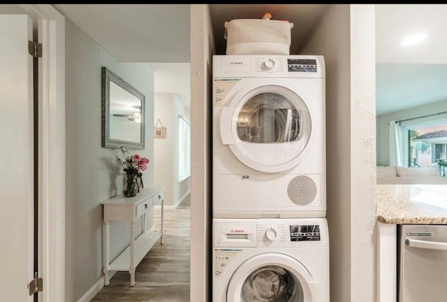 laundry room with baseboards, wood finished floors, stacked washer and clothes dryer, and laundry area