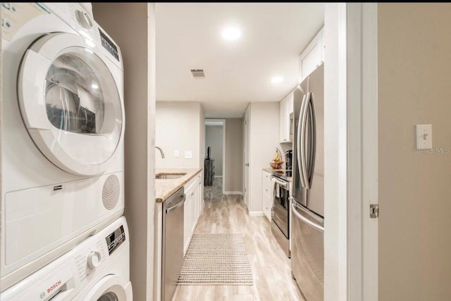 laundry area with a sink, light wood finished floors, stacked washing maching and dryer, laundry area, and visible vents