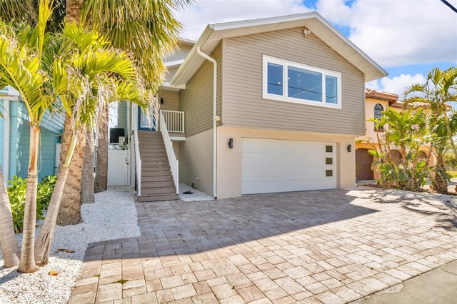 coastal inspired home with stucco siding, stairs, an attached garage, driveway, and central AC unit