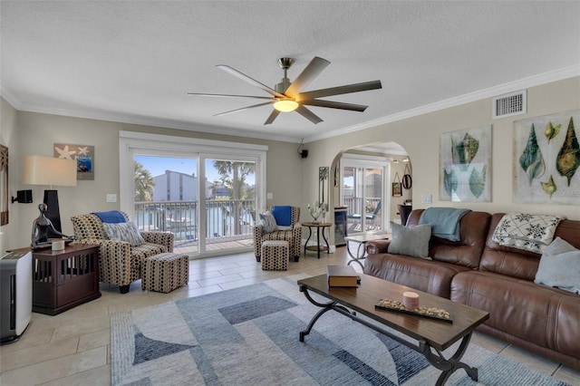 living room featuring light tile patterned flooring, visible vents, ceiling fan, ornamental molding, and arched walkways