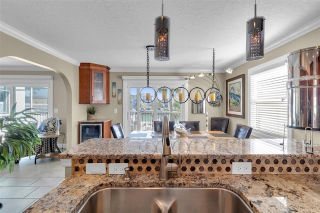 kitchen with ornamental molding, a sink, light stone counters, pendant lighting, and beverage cooler