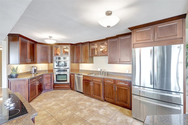 kitchen featuring light tile patterned flooring, glass insert cabinets, a sink, stone counters, and stainless steel appliances