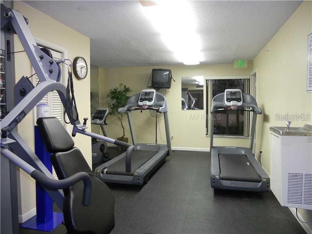 exercise room with a textured ceiling and baseboards