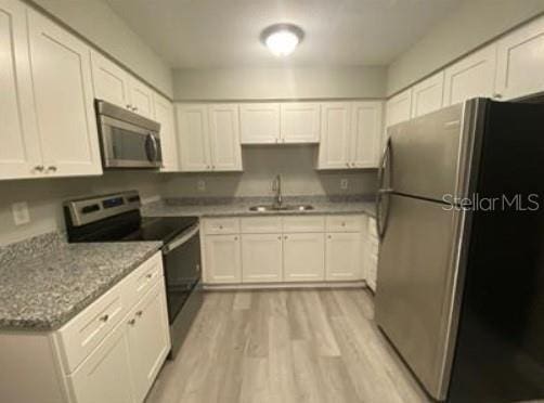 kitchen featuring light stone counters, a sink, appliances with stainless steel finishes, light wood-type flooring, and white cabinets