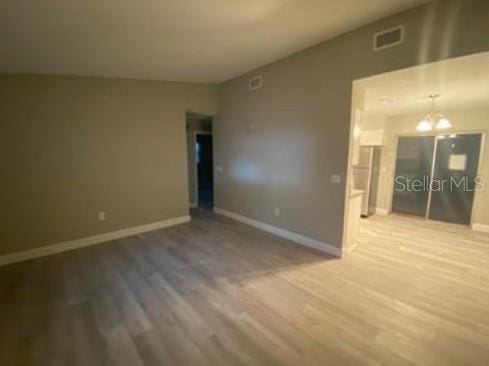 empty room with baseboards, visible vents, wood finished floors, and an inviting chandelier