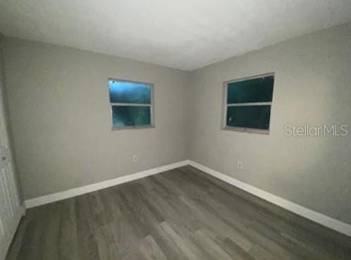 unfurnished room with dark wood-type flooring and baseboards